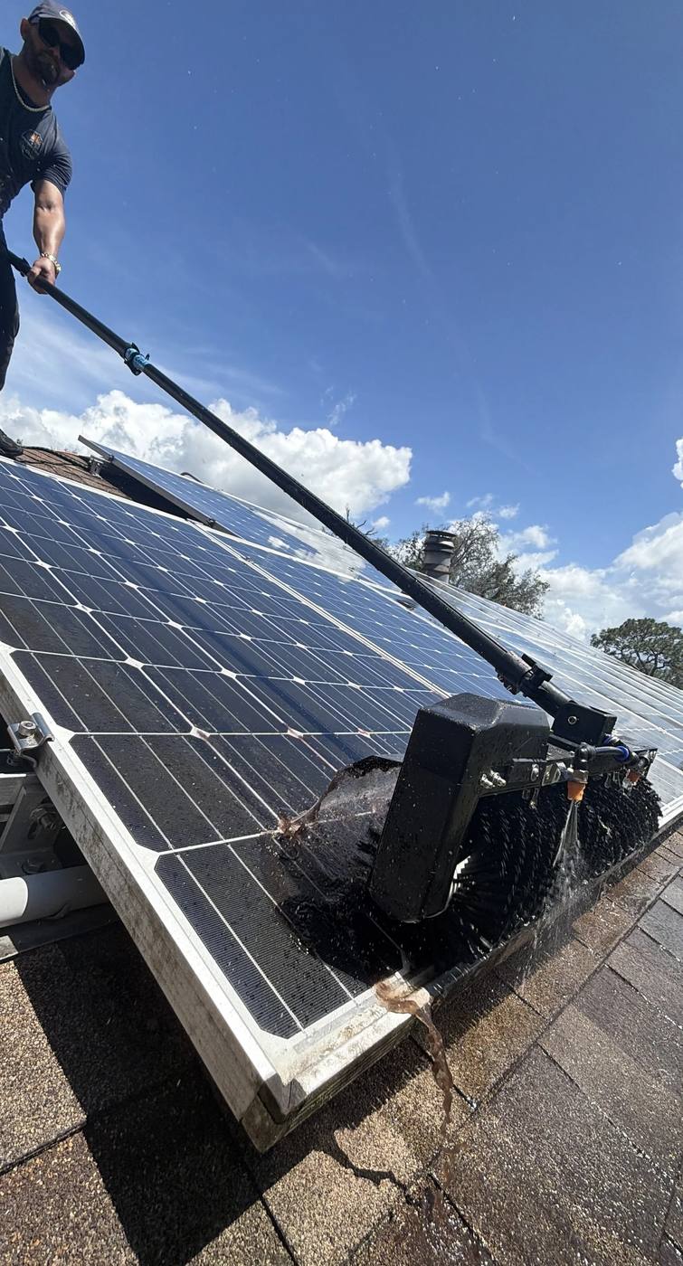 Motorized rotary brush cleaning a row of solar panels on a shingle roof